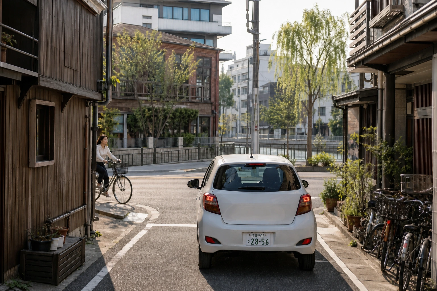 細い生活道路から大通りへ出ようとする江東ナンバーの車と、建物の陰から近づく自転車